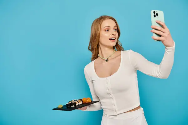 Mulher loira tirando uma selfie com seu telefone celular enquanto segura deliciosa comida asiática, marcando uma pose. — Fotografia de Stock