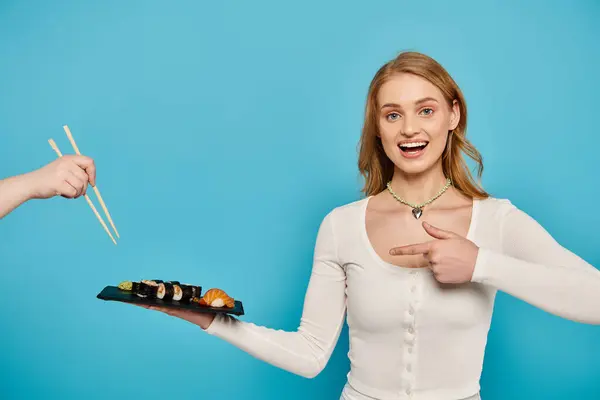 Blonde woman gracefully holds sushi plate, ready to enjoy Asian delicacy with chopsticks. — Stock Photo