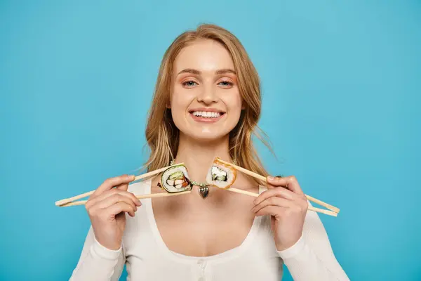 Une femme blonde tient délicatement deux baguettes avec des sushis perchés dessus, mettant en valeur l'art élégant de savourer la cuisine japonaise. — Photo de stock