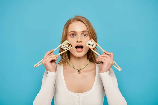 Eine schöne Frau mit blonden Haaren hält zwei Essstäbchen über ihren Augen in einer verspielten und künstlerischen Pose. — Stockfoto