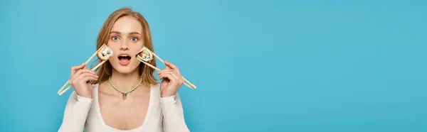 A beautiful woman with blonde hair holds up chopsticks with sushi near her face — Stock Photo