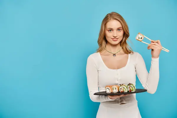 A beautiful woman with blonde hair delicately holds a plate filled with delicious sushi rolls. — Stock Photo