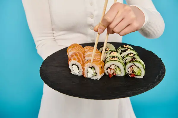 Vista recortada de una hermosa mujer sosteniendo un plato negro lleno de deliciosos rollos de sushi. - foto de stock