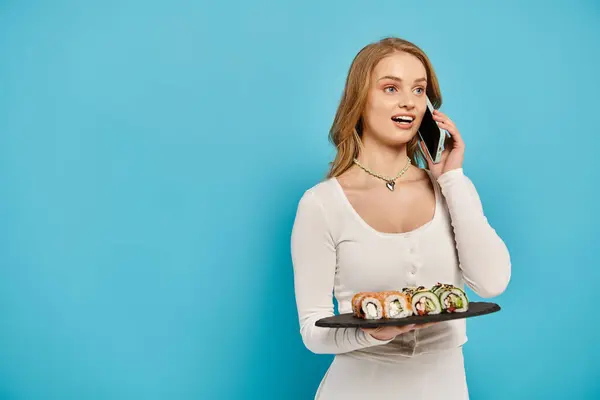 Una mujer rubia impresionante mostrando una bandeja llena de deliciosos rollos de sushi de una manera elegante y artística. - foto de stock
