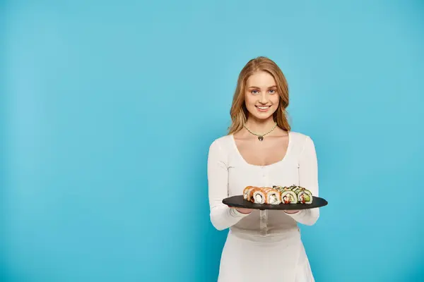 A beautiful blonde woman delicately holds a plate of colorful sushi rolls, showcasing the delicious Asian cuisine. — Stock Photo