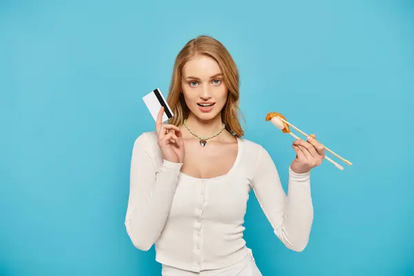 Une femme blonde tient gracieusement un morceau de nourriture asiatique avec des baguettes, mettant en valeur la finesse culinaire, carte de crédit. — Photo de stock