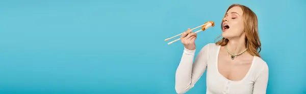 Una mujer con el pelo rubio sosteniendo palillos con sushi delicioso. - foto de stock