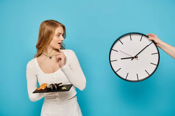 Жінка з білявим волоссям тримає тарілку азіатської їжі перед годинником, демонструючи спокусливий час їжі. — стокове фото