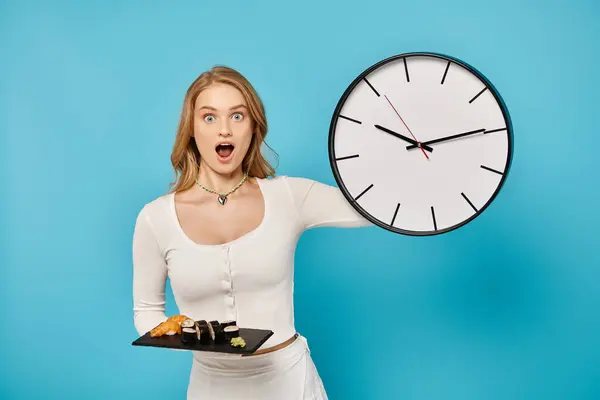 Una hermosa mujer con cabello rubio sosteniendo un plato de sushi con un diseño de reloj - foto de stock