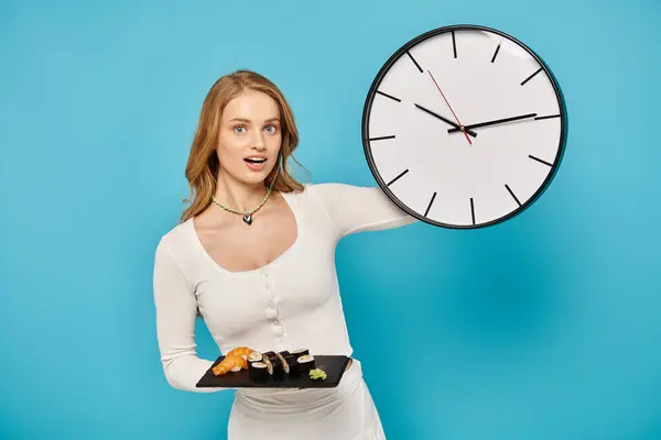 Una donna con i capelli biondi tiene un orologio in una mano e un piatto di cibo asiatico nell'altra, mostrando un equilibrio tra tempo e indulgenza.. — Foto stock