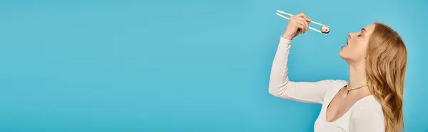 Una donna elegante con i capelli biondi tiene con grazia le bacchette con il sushi in mano. — Foto stock
