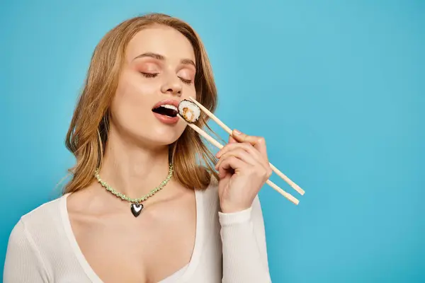 Une femme blonde élégante tient gracieusement deux baguettes entre ses lèvres, montrant son amour pour la cuisine asiatique. — Photo de stock