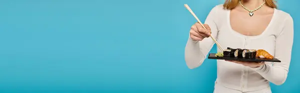 Cropped view of woman elegantly holding chopsticks and a plate of sushi. — Stock Photo