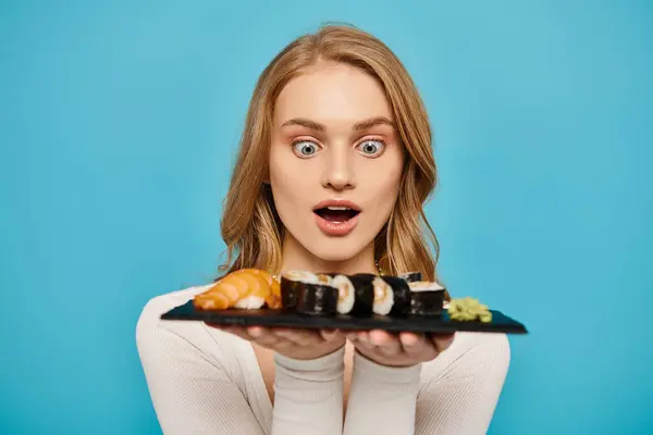 Une belle femme blonde tient gracieusement une assiette remplie de sushis colorés et appétissants. — Photo de stock