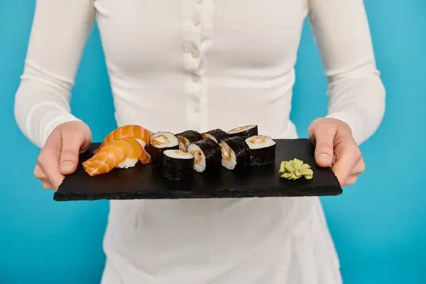 Vista recortada de mujer con cabello rubio sostiene una bandeja de sushi deliciosa, exudando gracia y sofisticación en un vestido blanco. - foto de stock