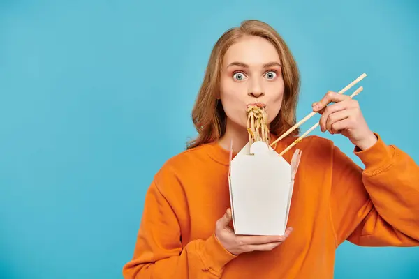 Una bella donna con i capelli biondi tiene delicatamente le bacchette davanti alla bocca, assaporando una deliziosa cucina asiatica. — Foto stock