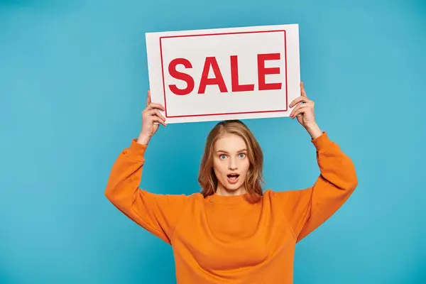 A stylish woman with blonde hair holds up a sign that reads sale — Stock Photo