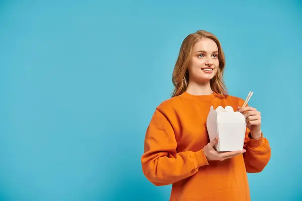 A stylish woman in an orange sweater delicately holds box of Asian food, exuding elegance and poise. — Stock Photo