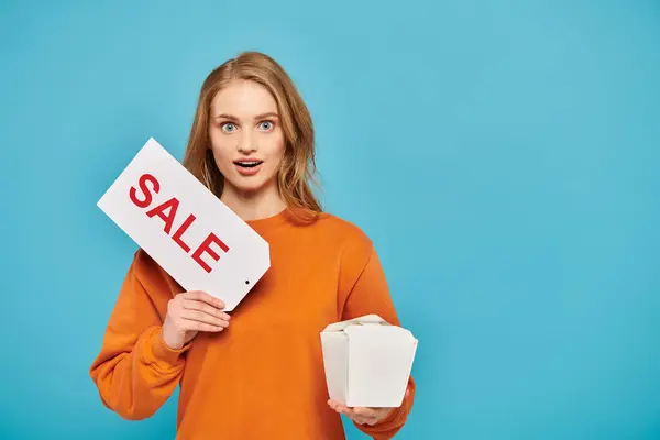 A stylish blonde woman confidently holds a sign that reads sale, showcasing Asian food in hand. — Stock Photo