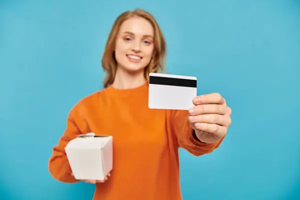 Una mujer con estilo tiene una tarjeta de crédito y una caja, mostrando un estilo de vida moderno y el consumismo. - foto de stock
