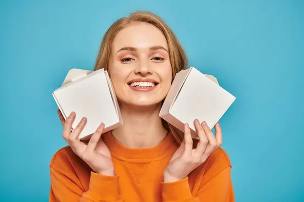Uma bela mulher loira segura duas caixas de comida na frente de seu rosto, escondendo sua expressão com intriga. — Fotografia de Stock