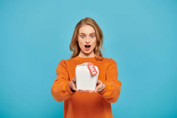 A beautiful blonde woman holding a food box, looking surprised. — Stock Photo