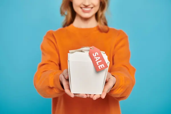 Vue recadrée d'une femme élégante tenant une boîte à nourriture avec une étiquette de vente, ravie et intriguée par le contenu. — Photo de stock
