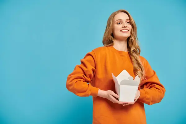 A lovely woman in an orange sweater elegantly holds a box of delicious Asian food. — Stock Photo