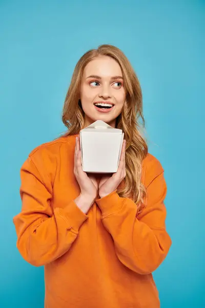A beautiful blonde woman holding a food box with a surprised expression. — Stock Photo