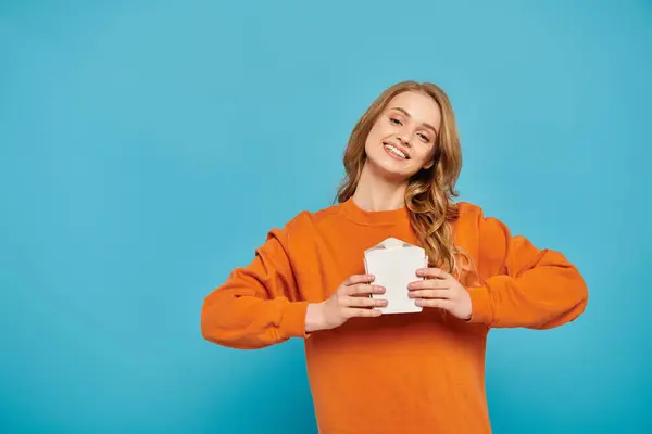 A stylish woman in an orange sweater enjoying a moment of relaxation while holding food box. — Stock Photo