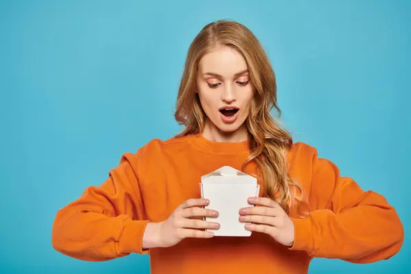 Eine atemberaubende blonde Frau in orangefarbenem Pullover hält eine weiße Lebensmittelbox in der Hand — Stockfoto
