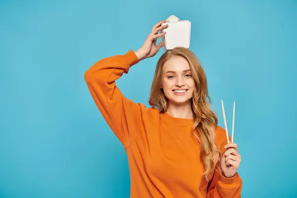 Une femme blonde dans un pull orange posant sereinement avec de la nourriture asiatique. — Photo de stock