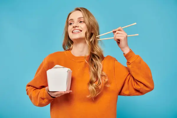A blonde woman gracefully holds chopsticks and a box of Asian food, showcasing a blend of beauty and culinary artistry. — Stock Photo
