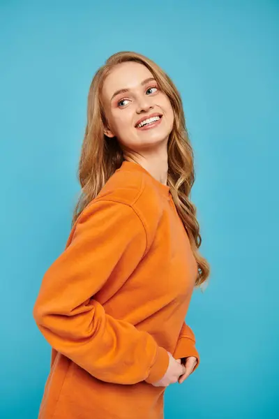 A graceful woman in an orange sweater posing on blue vibrant backdrop. — Stock Photo
