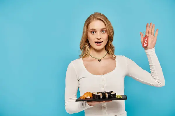 Eine blonde Frau hält anmutig ein Tablett mit asiatischer Küche mit einem Verkaufsschild in der Hand. — Stockfoto