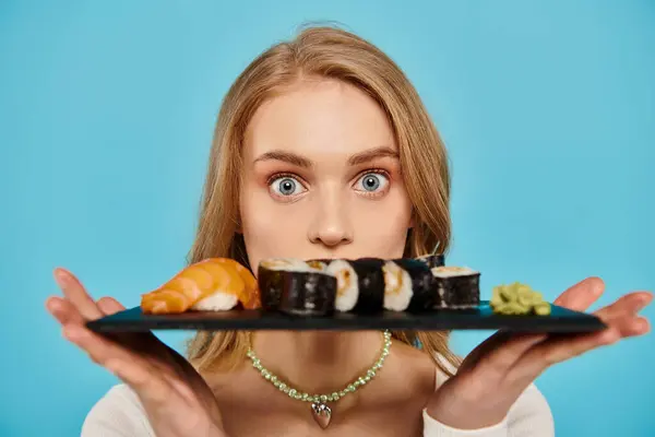 Une belle femme blonde tient gracieusement une assiette remplie d'une variété de sushis, mettant en valeur la délicieuse cuisine asiatique. — Photo de stock