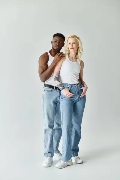 A young multicultural couple standing together in a studio against a grey background, showcasing unity and diversity. — Stock Photo