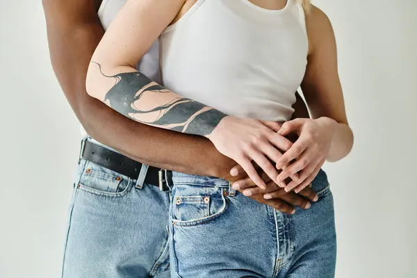 Um homem com uma tatuagem no braço segurando uma mão de mulher, mostrando unidade, amor e conexão entre um casal multicultural em um estúdio em um fundo cinza. — Fotografia de Stock