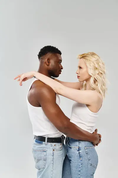 A young multicultural couple standing together on a grey background, embodying unity and connection through their presence. — Stock Photo