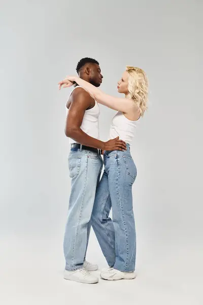 A young multicultural couple stands together, exuding a strong sense of unity and togetherness in a studio against a grey background. — Stock Photo