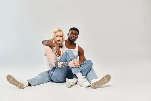 Un jeune homme et une jeune femme assis sur le sol, perdus dans la conversation et la connexion dans un contexte gris. — Photo de stock
