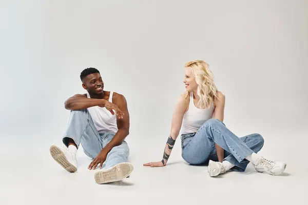 Un jeune couple multiculturel assis paisiblement et relié par terre dans un décor de studio sur fond gris. — Photo de stock