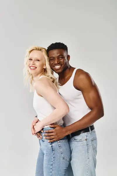 A young multicultural couple striking a pose together in a studio against a grey background. — Stock Photo