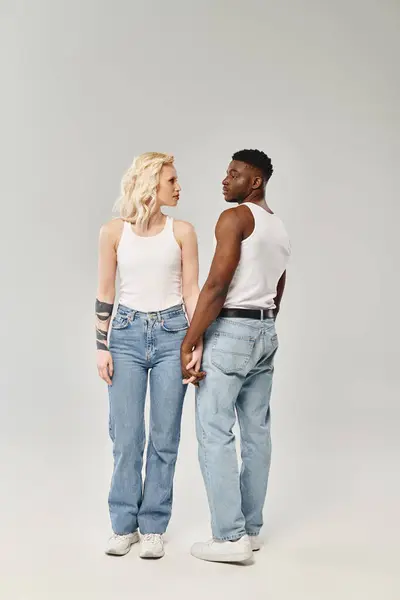 Um jovem casal multicultural está lado a lado em um estúdio contra um fundo cinza, mostrando unidade e união. — Fotografia de Stock