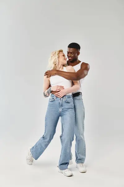 A young multicultural couple sharing a warm and tender hug in a studio, against a grey background. — Stock Photo