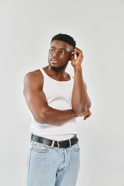 Ein junger, sexy afroamerikanischer Mann in weißem Tank-Top, der in einem Studio vor grauem Hintergrund mit einem Handy spricht. — Stockfoto