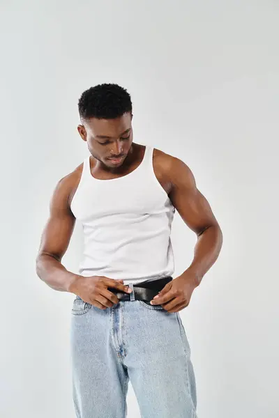 Un jeune Afro-Américain en débardeur blanc posant sur fond de studio gris. — Photo de stock