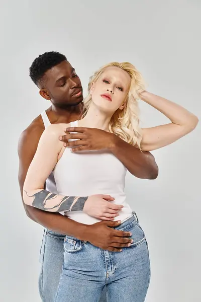 Un homme tient tendrement une femme dans ses bras, exprimant amour et intimité. Ils sont un jeune couple interracial sur fond de studio gris. — Photo de stock