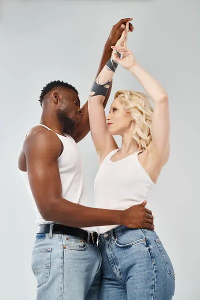 A young interracial couple dancing gracefully together in a studio against a grey background. — Stock Photo