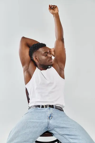 Un jeune homme de descendance interracial dans un débardeur blanc se balançant sur ses mains dans un décor de studio sur fond gris. — Photo de stock